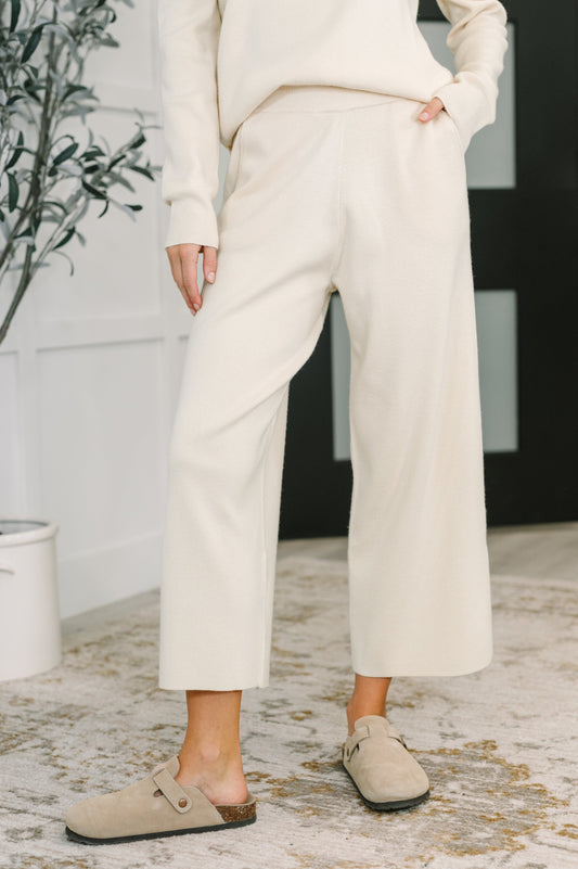 Person wearing a white outfit with wide-leg pants and beige shoes indoors.
