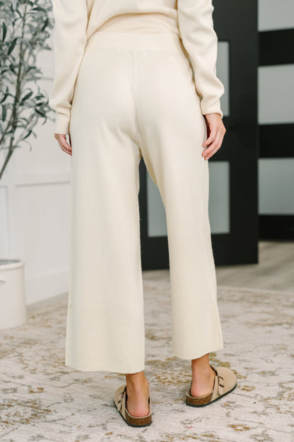 Person wearing a cream-colored outfit with wide-leg pants in an indoor setting.