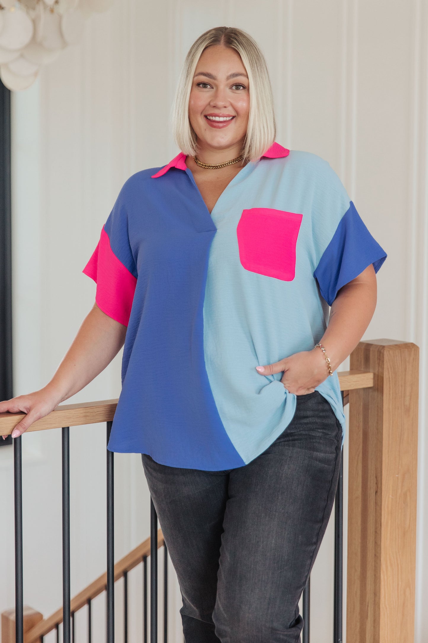 Woman wearing a colorful shirt with a pink pocket standing on a staircase.