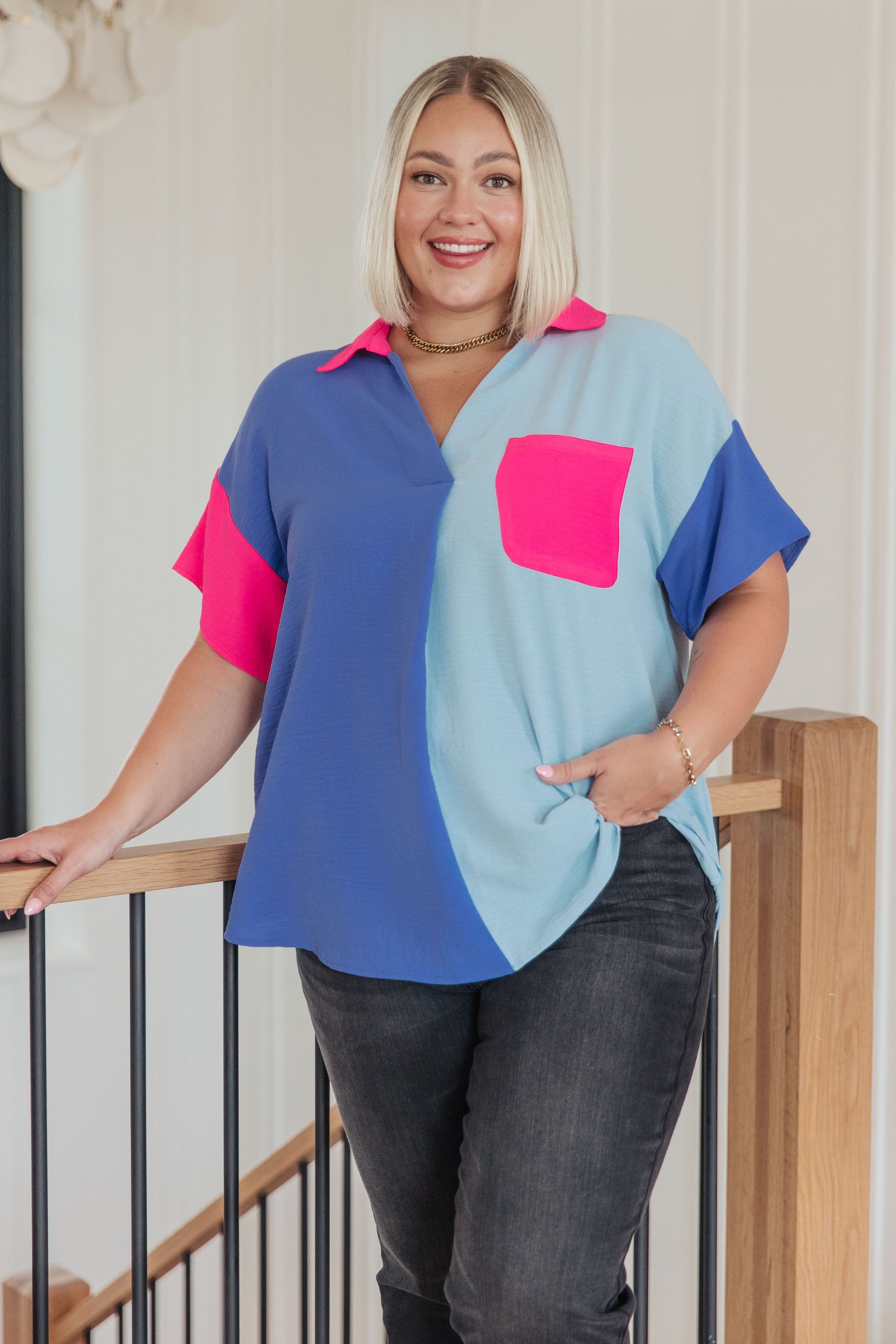 Woman wearing a colorful shirt with a pink pocket standing on a staircase.