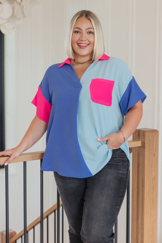Woman wearing a colorful shirt with a pink pocket standing on a staircase.