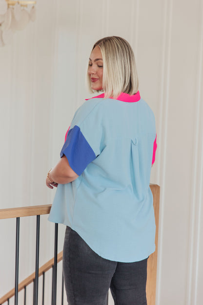 Woman wearing a light blue shirt with pink and purple sleeves in an indoor setting.