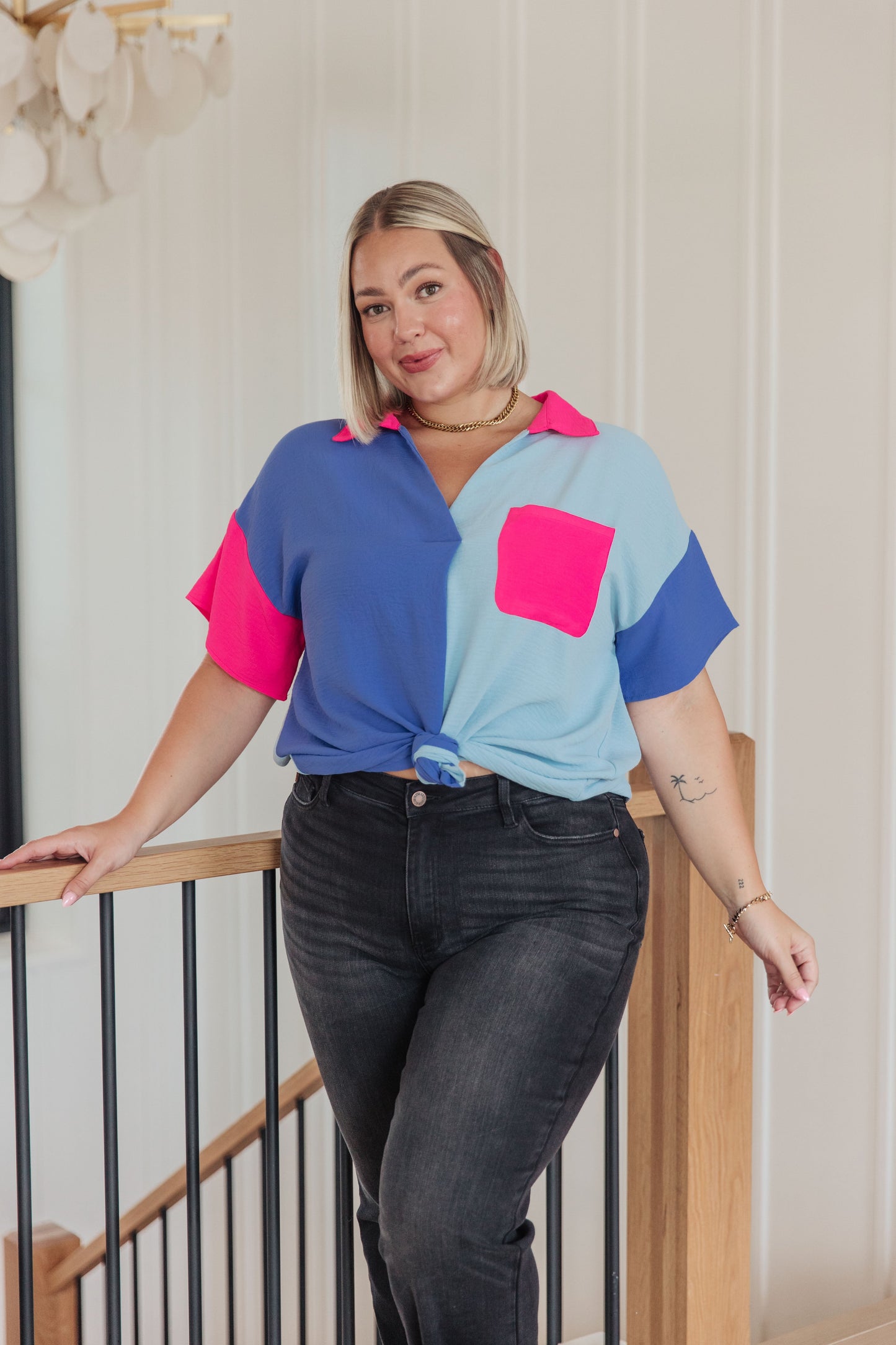 Woman wearing a colorful shirt and black jeans standing indoors.