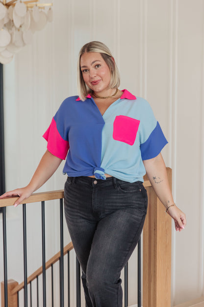 Woman wearing a colorful shirt and black jeans standing indoors.
