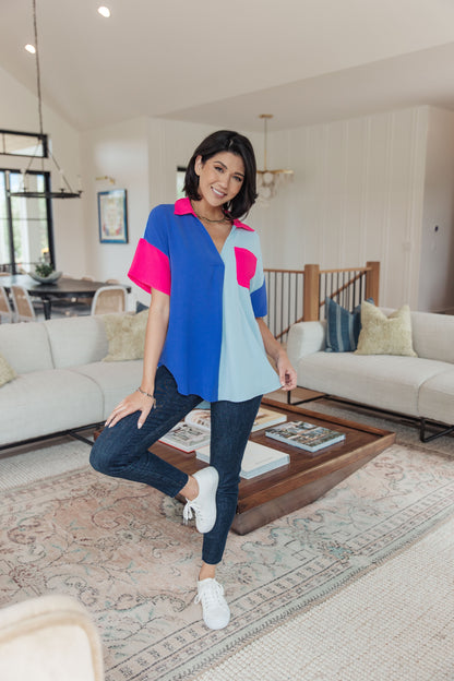 Woman posing in a modern living room with a colorful top and jeans.