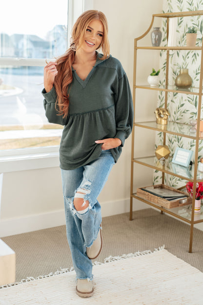Woman wearing a green oversized sweater and ripped jeans in a home setting.