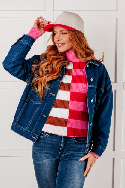 Woman wearing a denim jacket, checkered sweater, and red hat against a white background