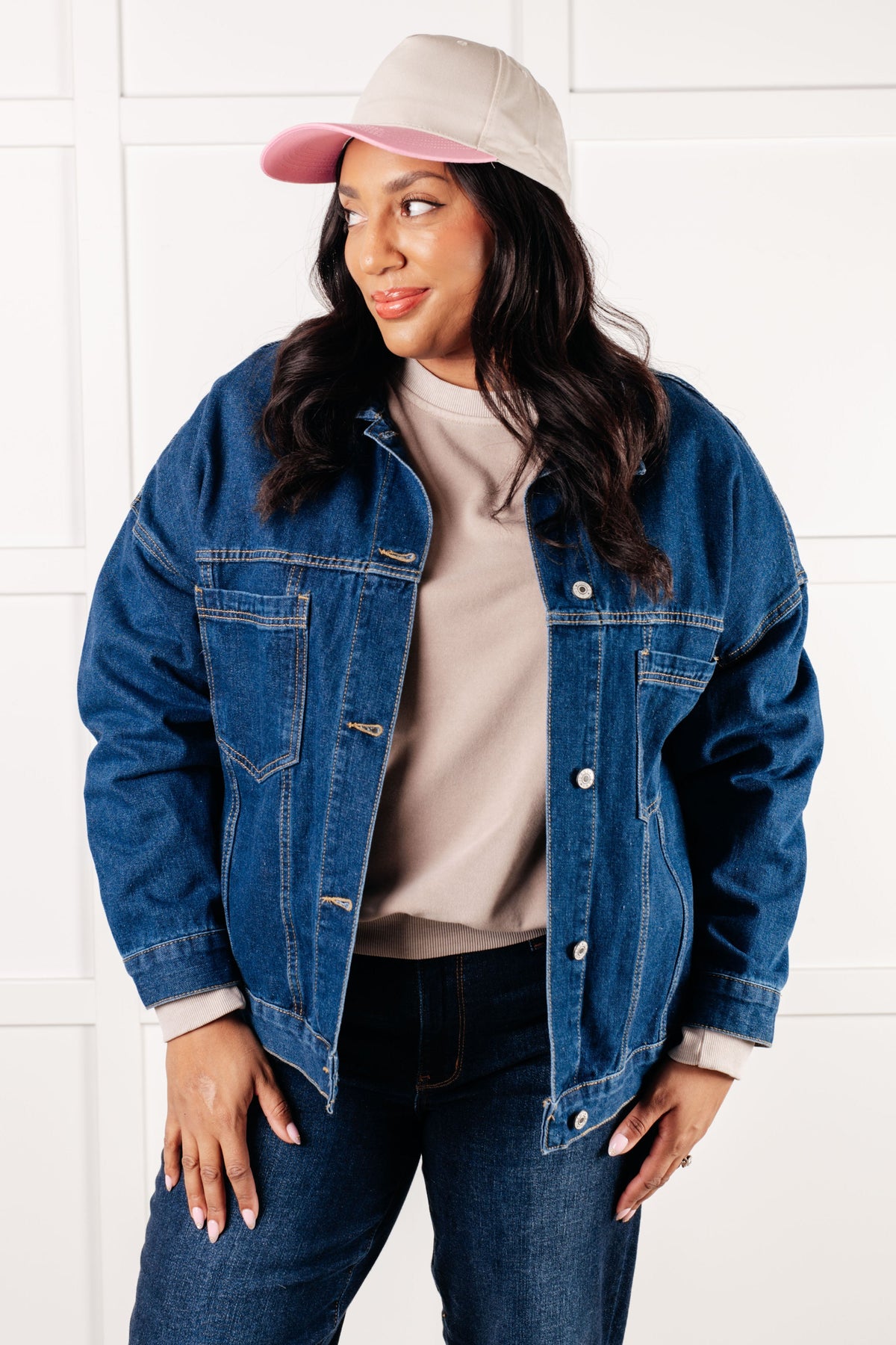 Woman wearing a blue denim jacket, white shirt, and pink cap against a white background