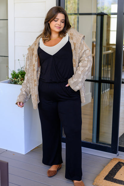 Woman wearing a beige cardigan, black top, and black pants on a patio.