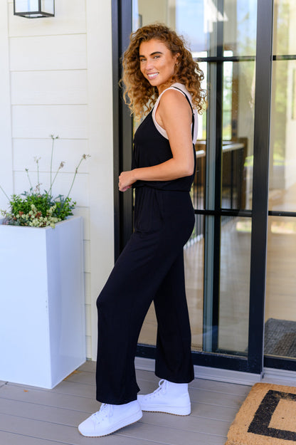 Woman in a black jumpsuit standing in front of a glass door.