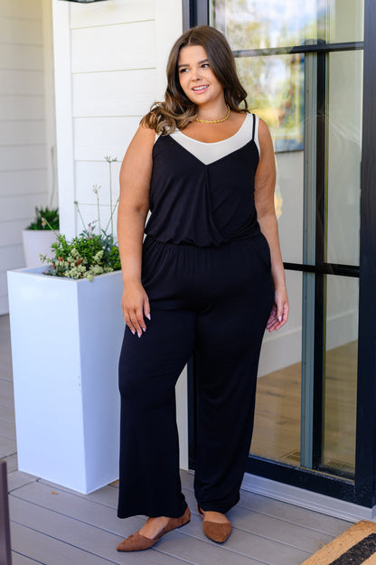 Woman wearing a black jumpsuit standing on a porch.