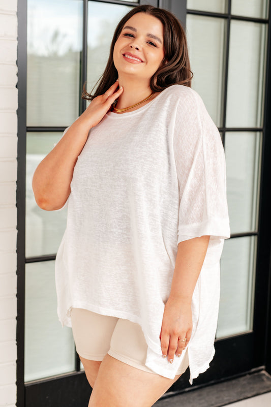 Woman wearing a white oversized shirt and beige shorts standing indoors.