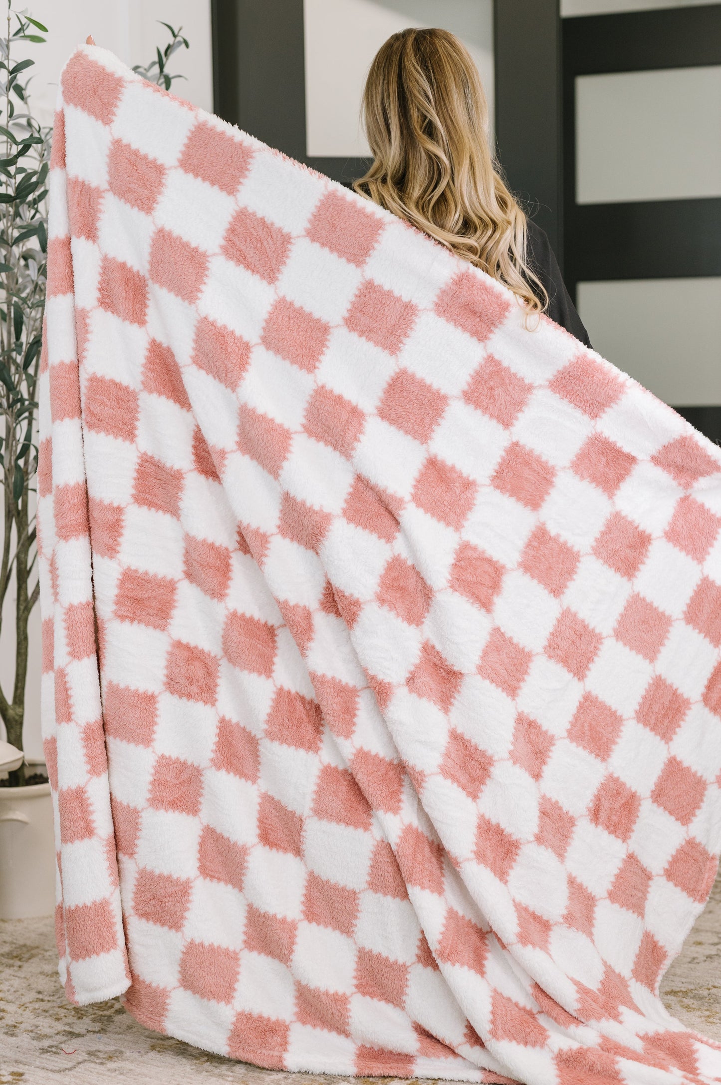 Person holding a pink and white checkered blanket indoors.