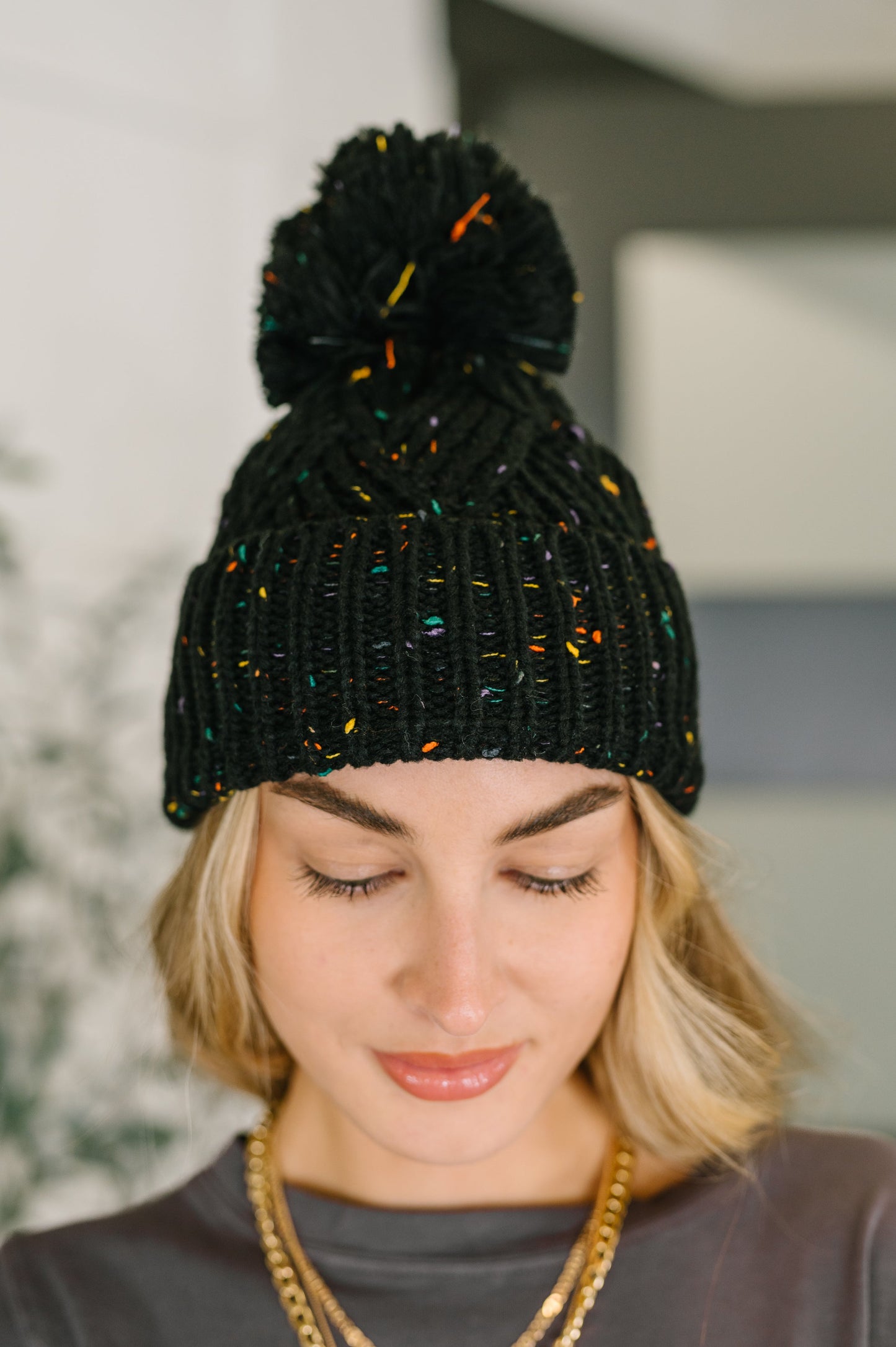 Person wearing a black knit beanie with colorful accents and a pom-pom.