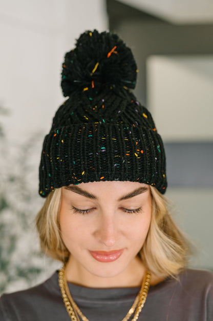 Person wearing a black knit beanie with colorful accents and a pom-pom.