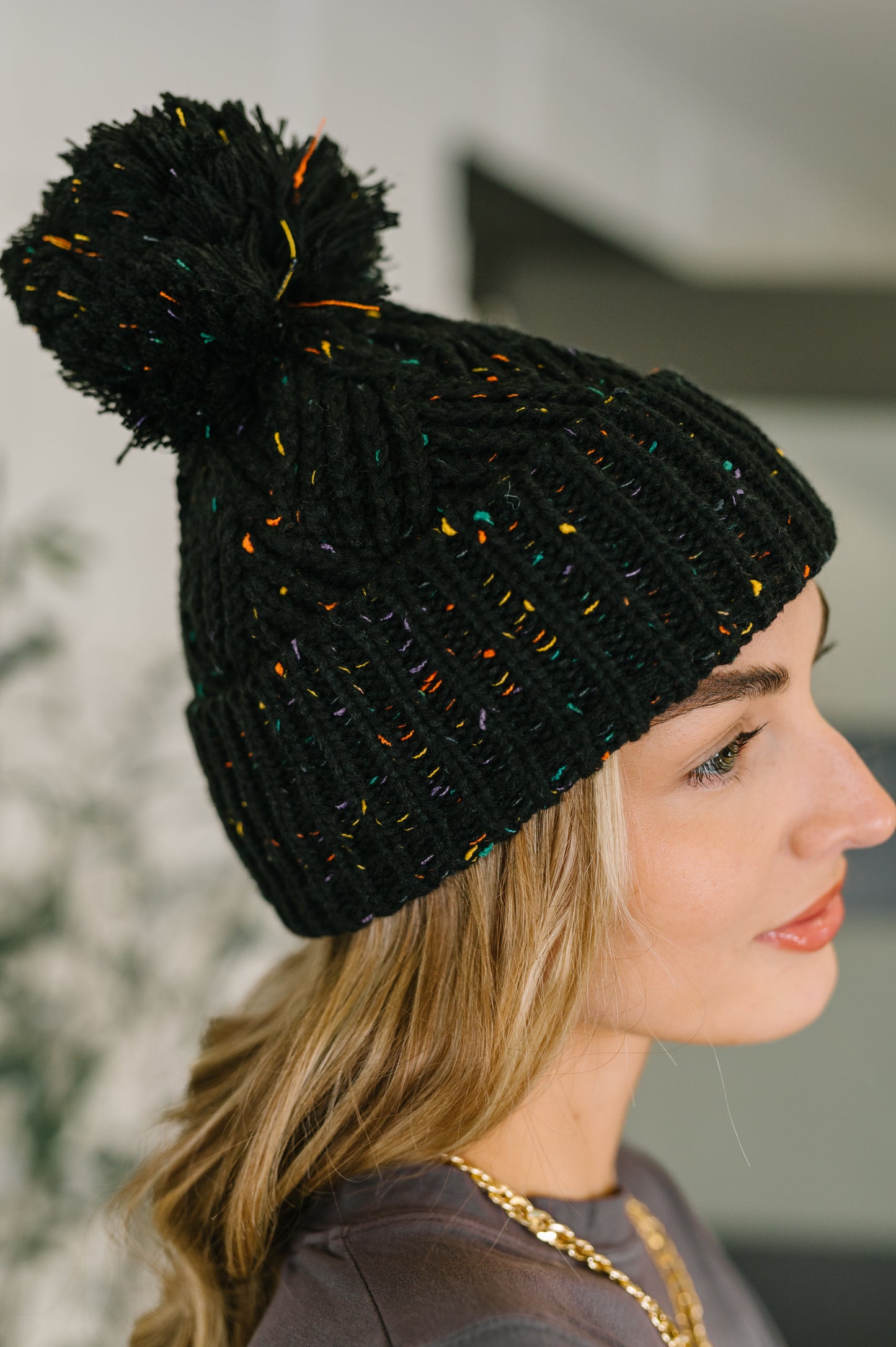 Woman wearing a black knit beanie with colorful pom-pom indoors