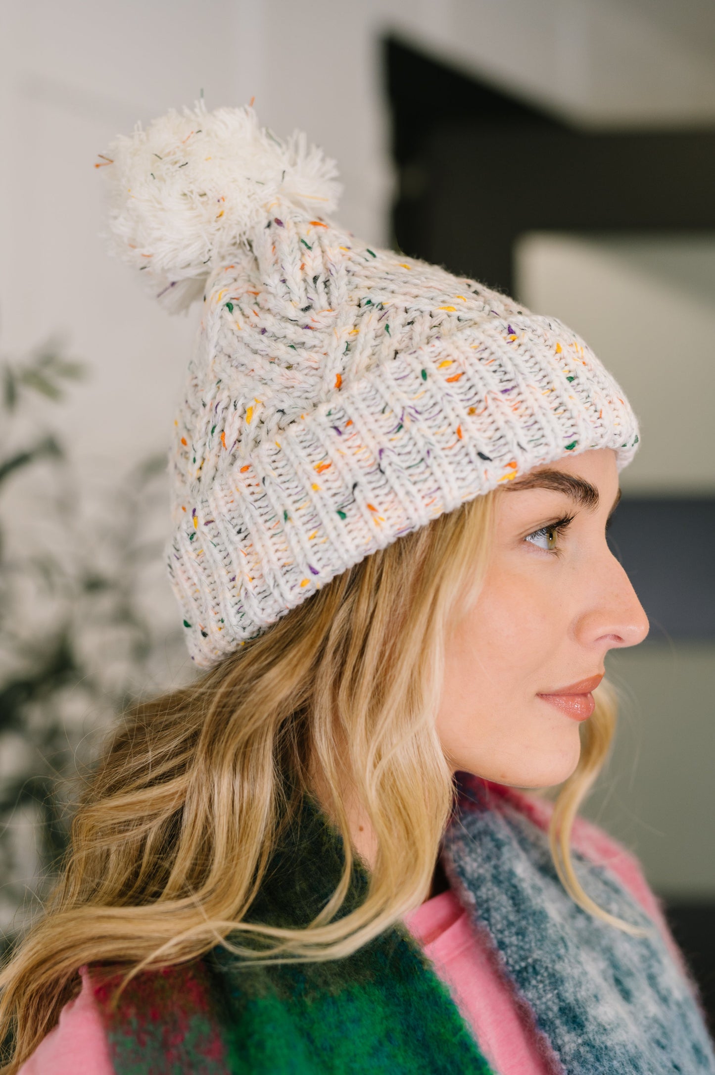 Woman wearing a colorful knit beanie with a pom-pom indoors.