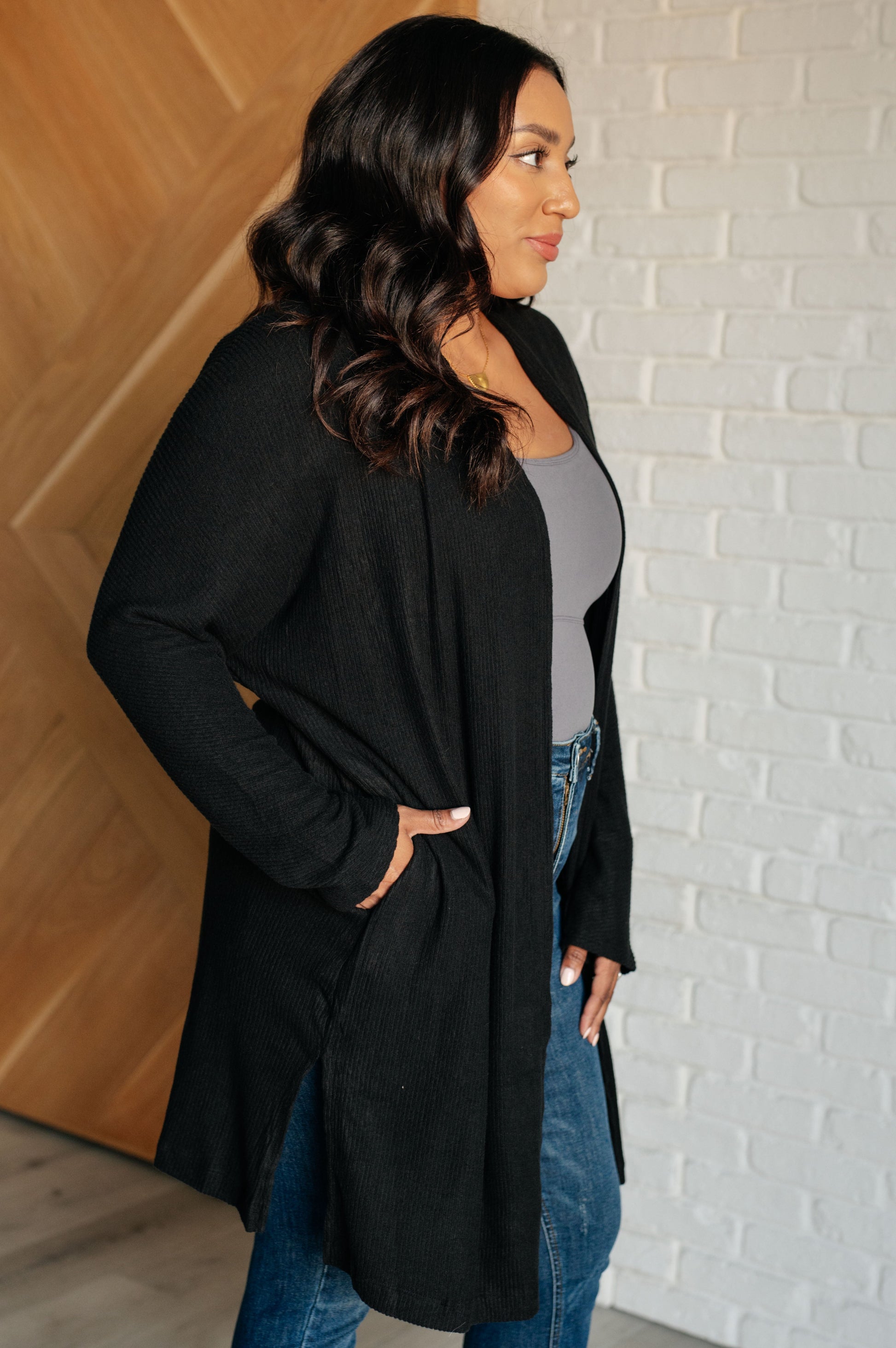 Woman wearing a black long coat against a white brick wall.