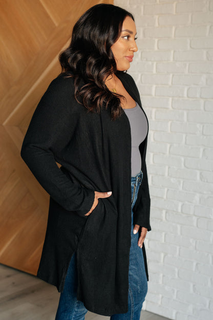 Woman wearing a black long coat against a white brick wall.