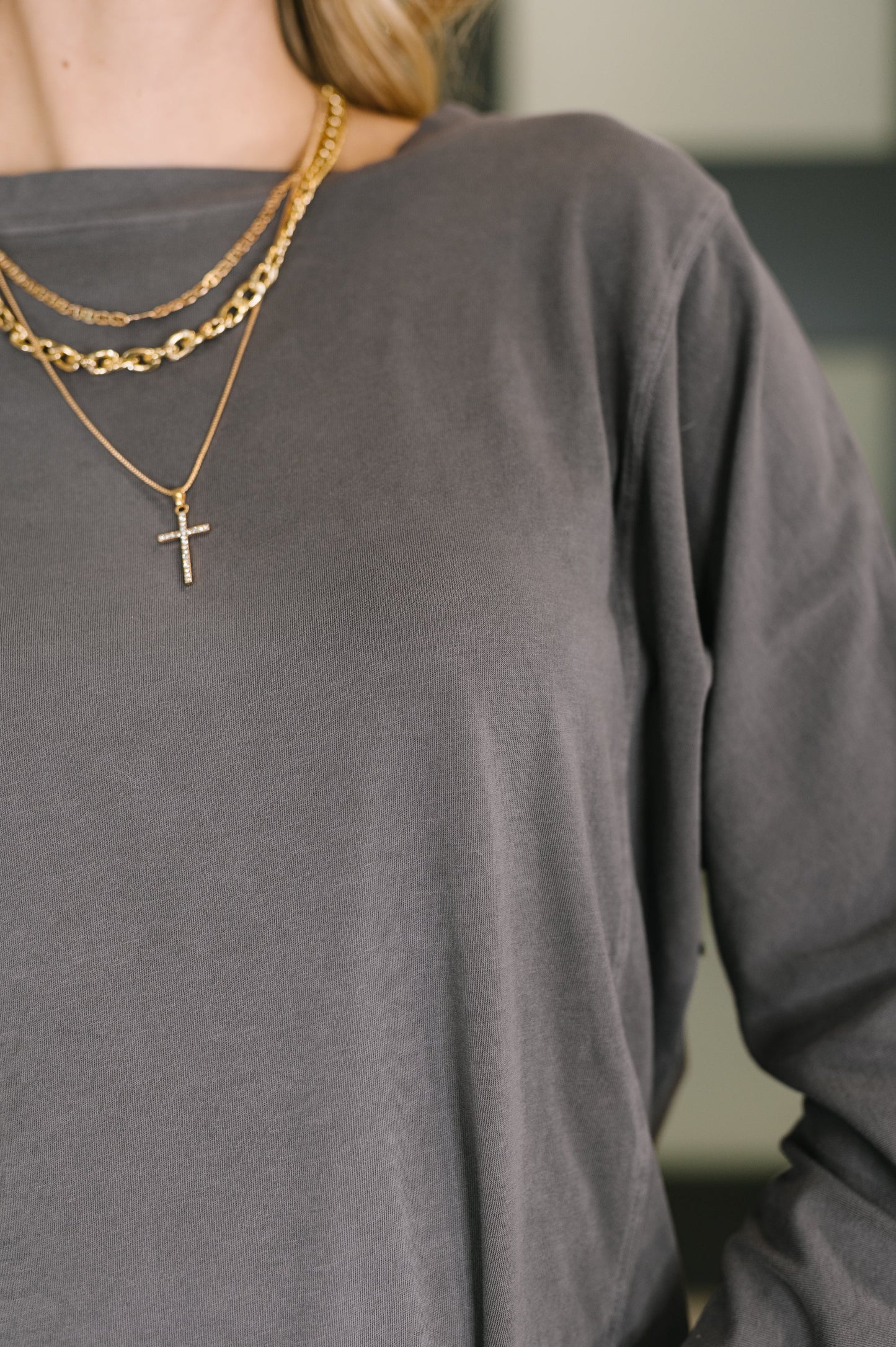 Person wearing a gray long-sleeve shirt with gold chain necklaces.