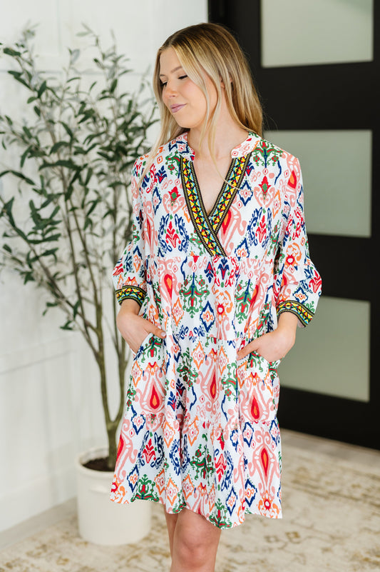 Woman wearing a colorful patterned dress standing indoors with a plant in the background