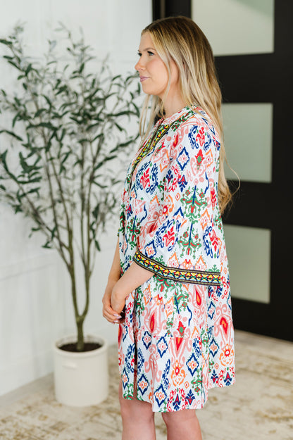 Woman wearing a colorful patterned dress standing indoors with a plant in the background