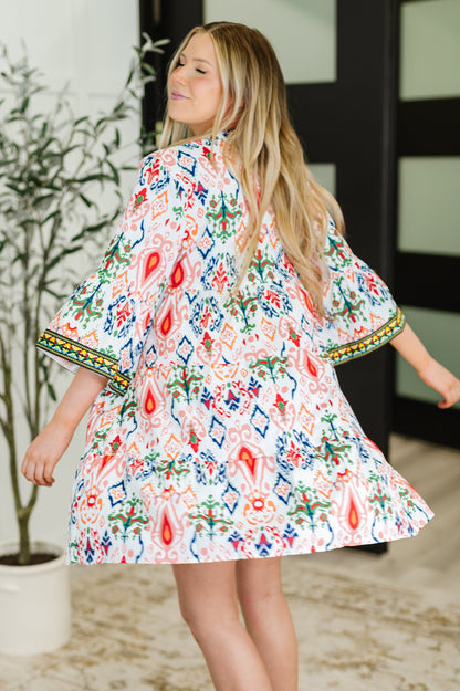 Woman wearing a colorful floral dress with bell sleeves indoors.