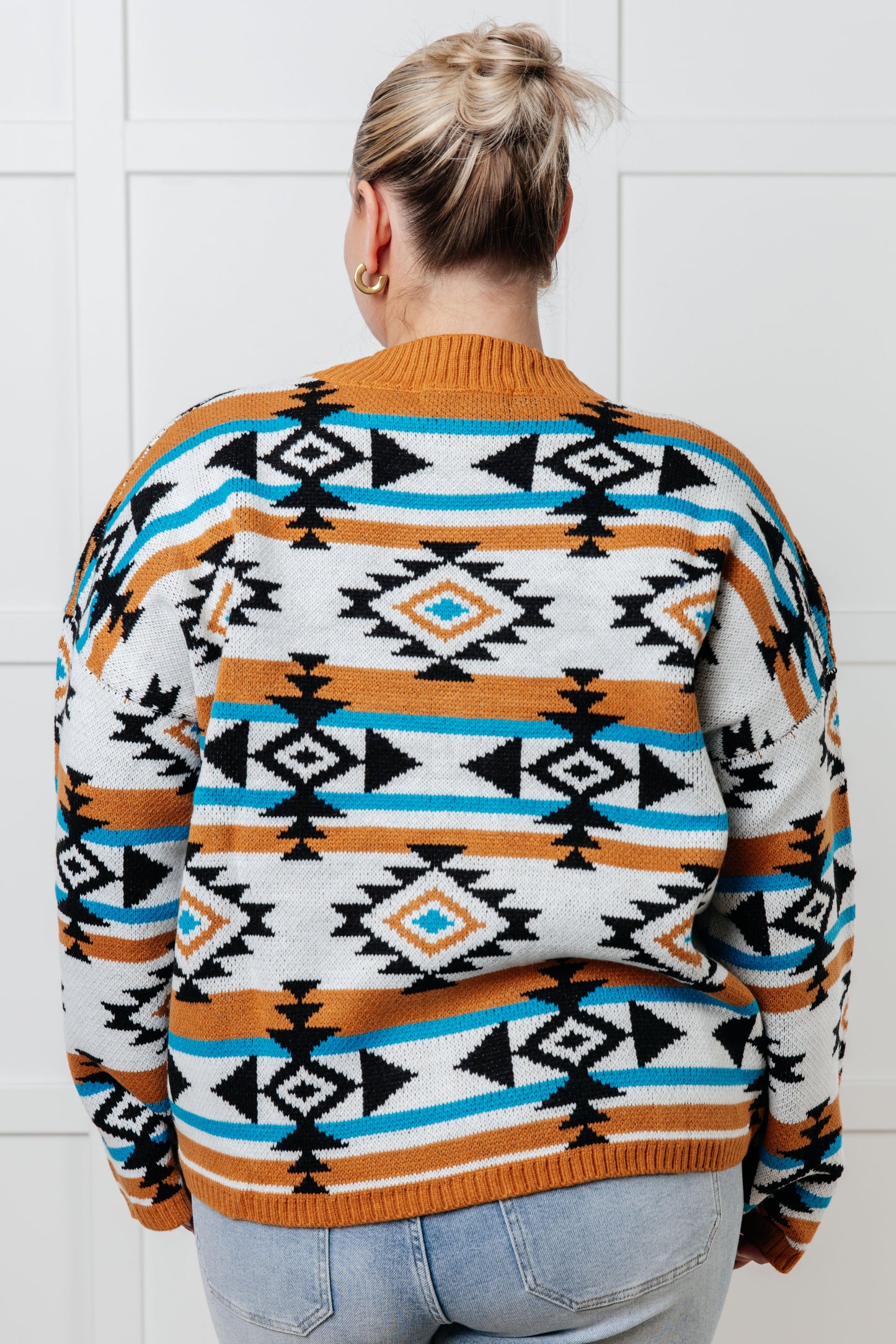 Person wearing a patterned sweater with a white tiled wall background