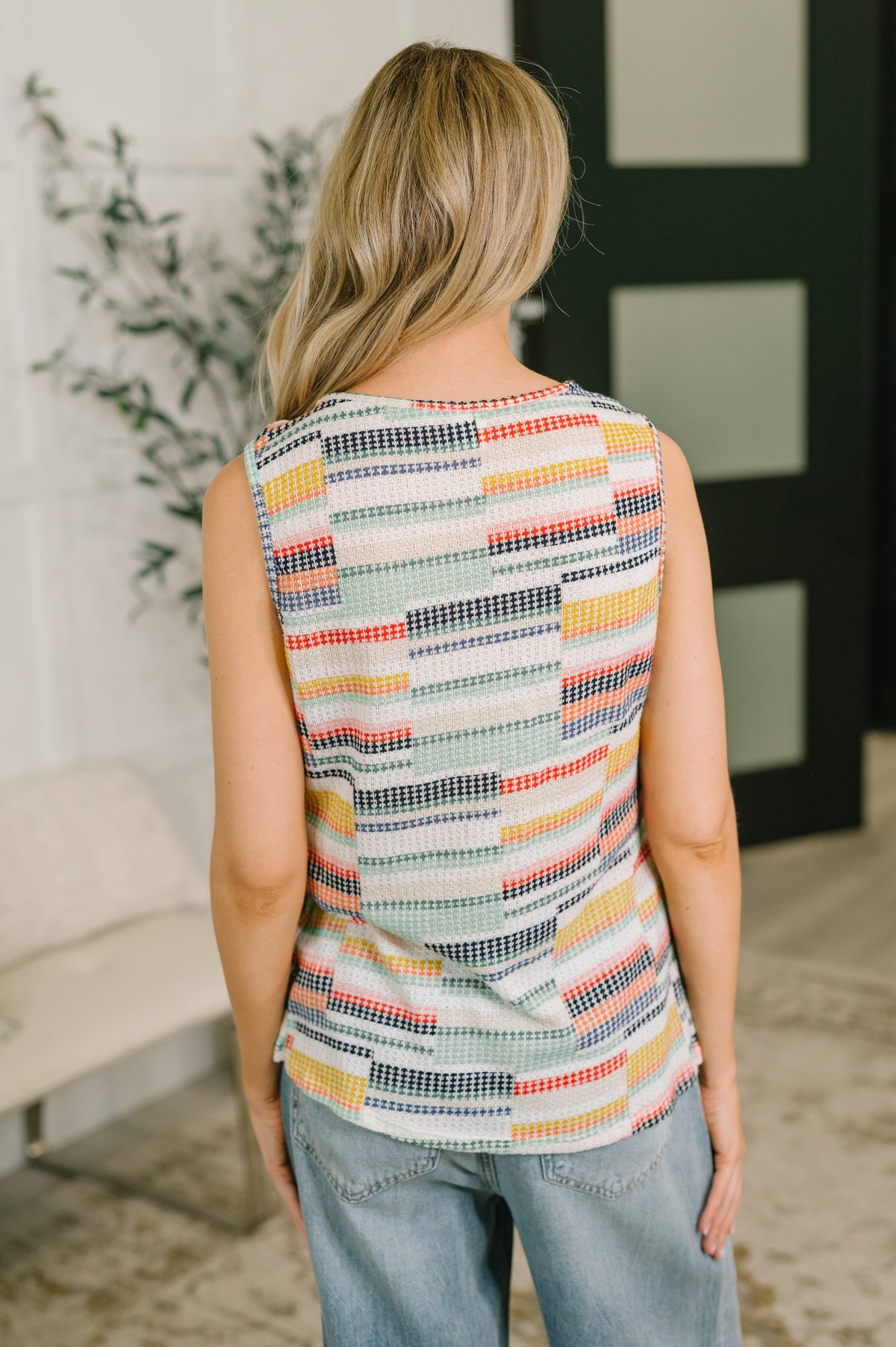Woman wearing a colorful striped sleeveless top in an indoor setting.