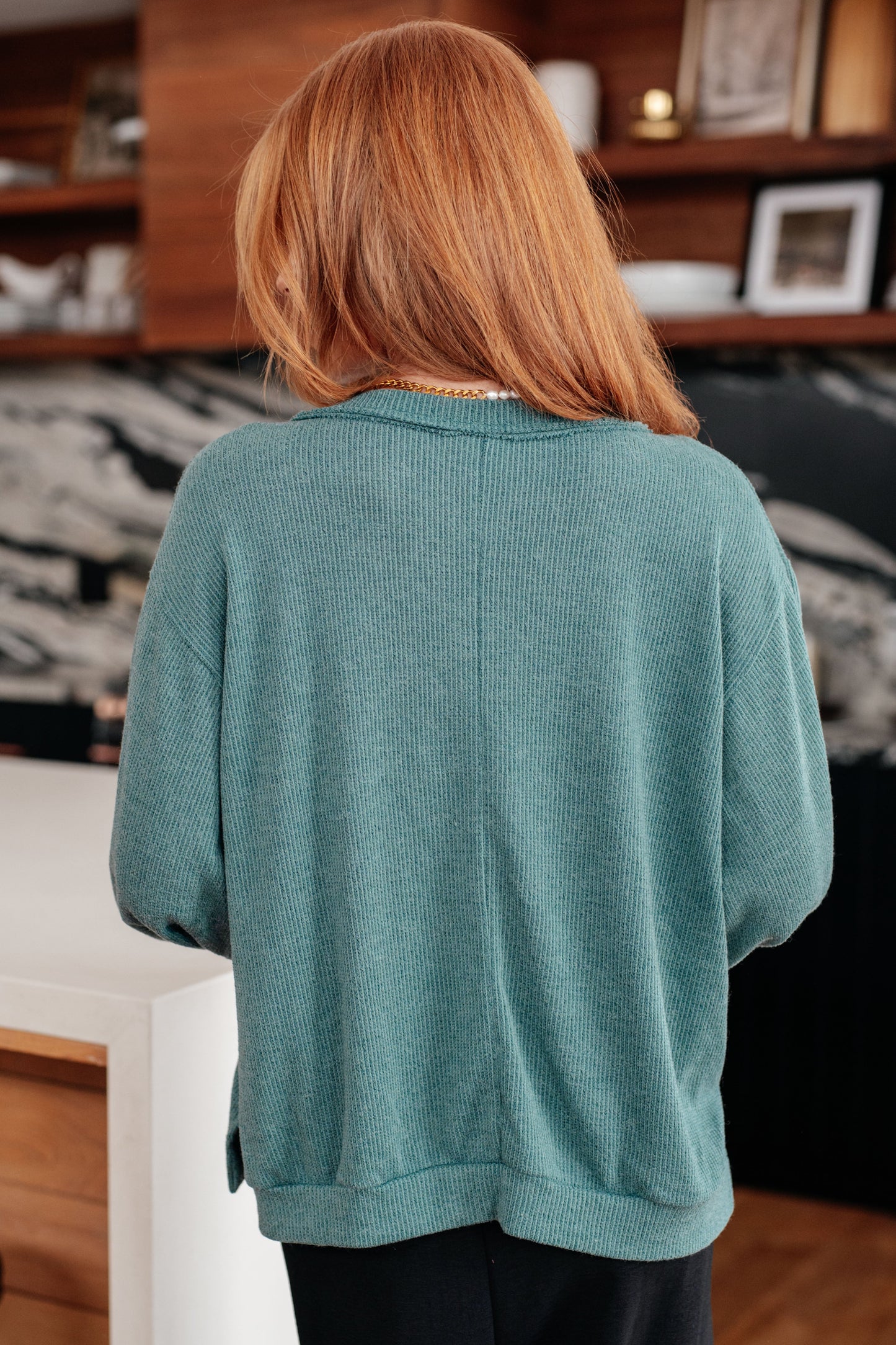 Person wearing a teal sweater in an indoor setting with a shelf in the background