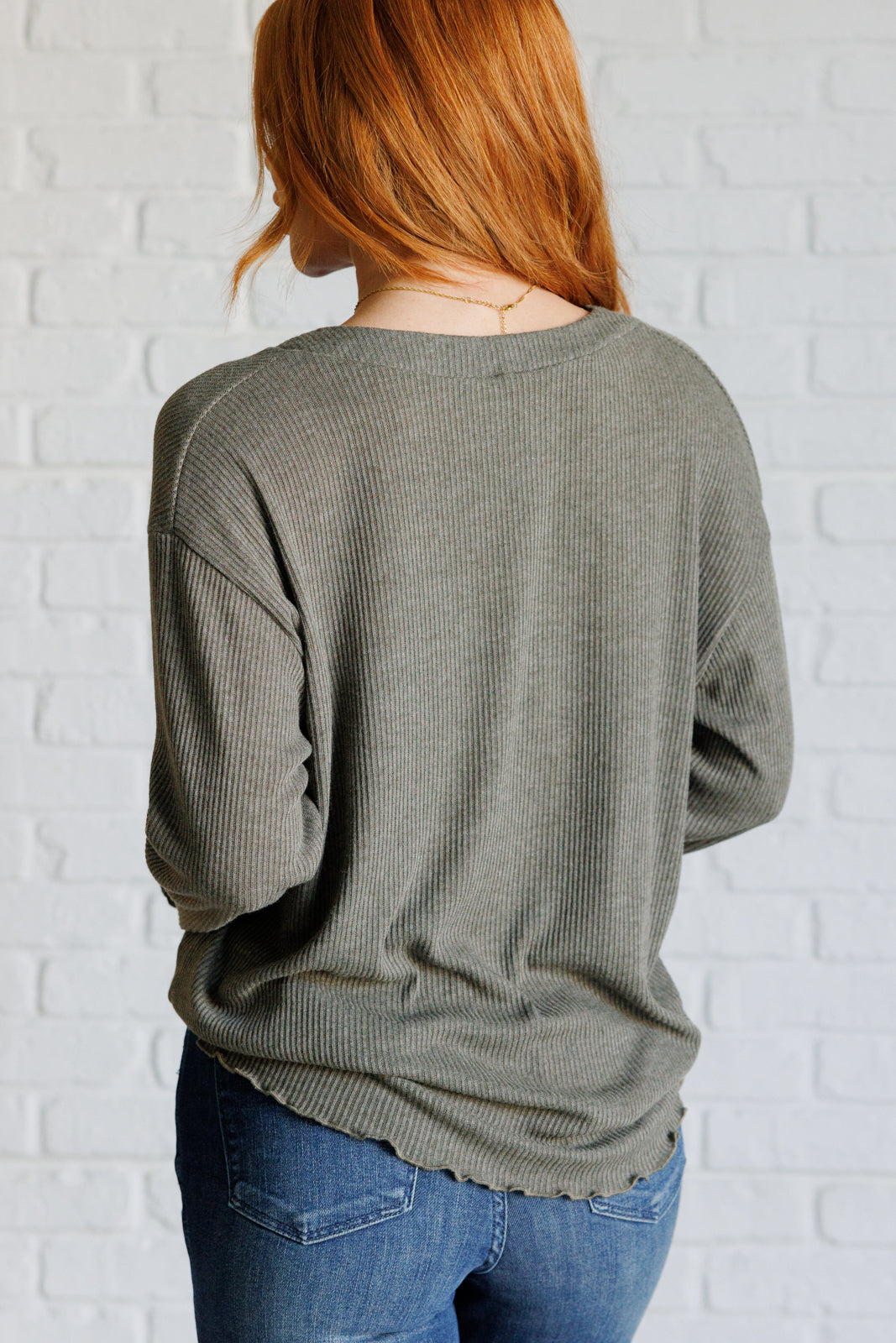 Person wearing a green sweater and blue jeans against a white brick wall