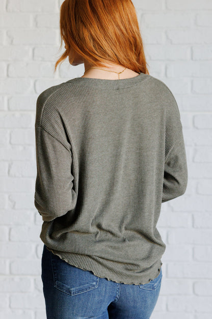 Person wearing a green sweater and blue jeans against a white brick wall