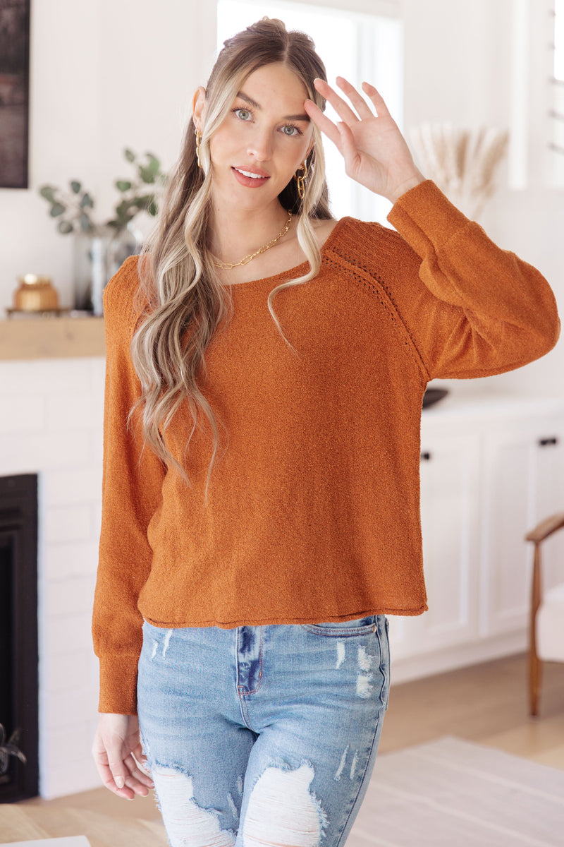 Woman wearing a rust-colored sweater and blue jeans in a home setting