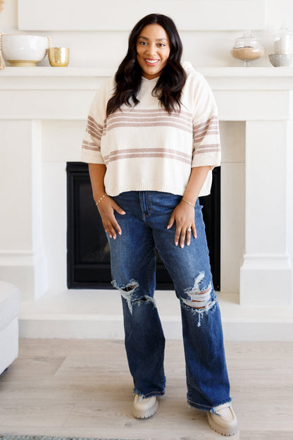 Woman wearing a striped sweater and jeans standing in a room with white walls and a fireplace.
