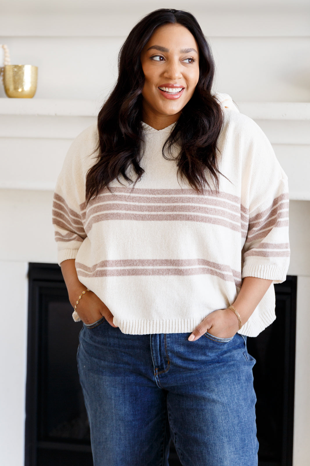 Woman wearing a striped sweater and jeans standing in front of a fireplace.