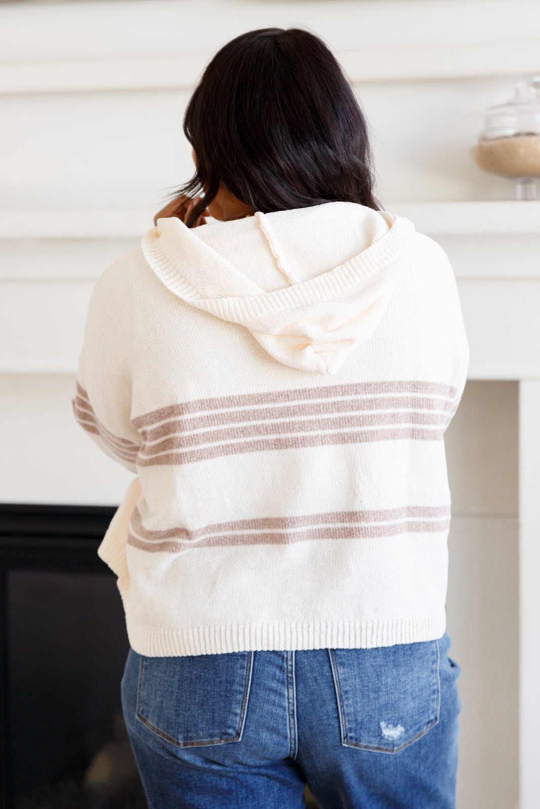 Person wearing a cream-colored hoodie with brown stripes from behind, standing in a room.