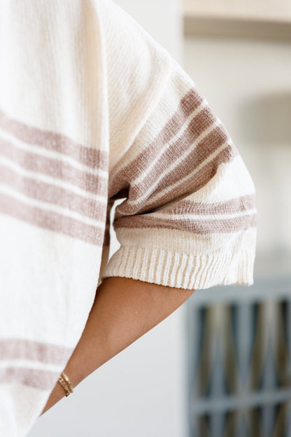 Close-up of a person wearing a beige and brown striped sweater with a blurred background