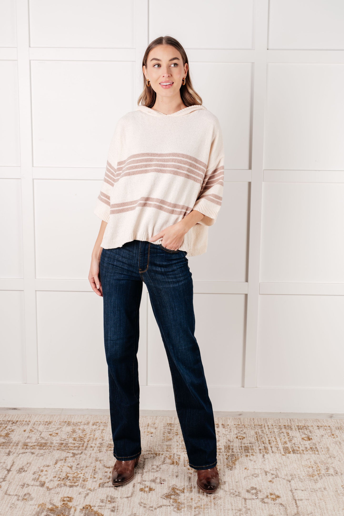 Woman wearing a striped sweater and jeans standing against a white tiled wall.