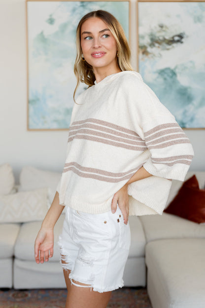 Woman wearing a white sweater with brown stripes and white shorts in a living room.
