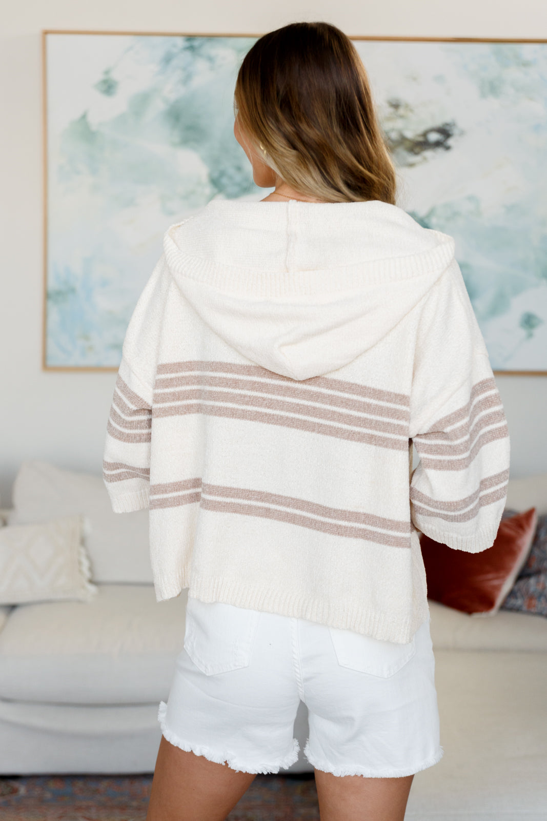 Woman wearing a white and beige striped hoodie and shorts in a living room setting.