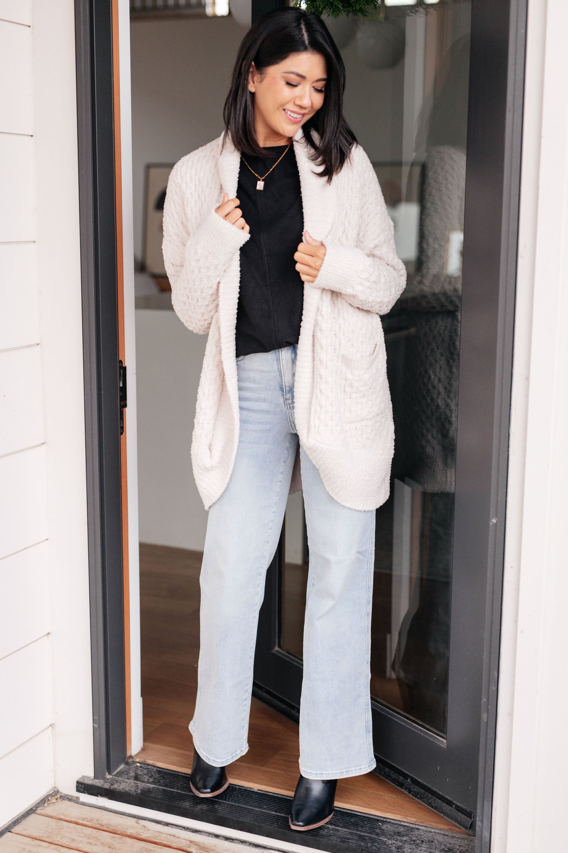 Woman wearing a white puffer coat, black top, and light blue jeans standing in a doorway.