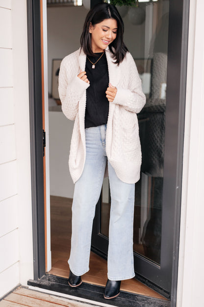 Woman wearing a white puffer coat, black top, and light blue jeans standing in a doorway.