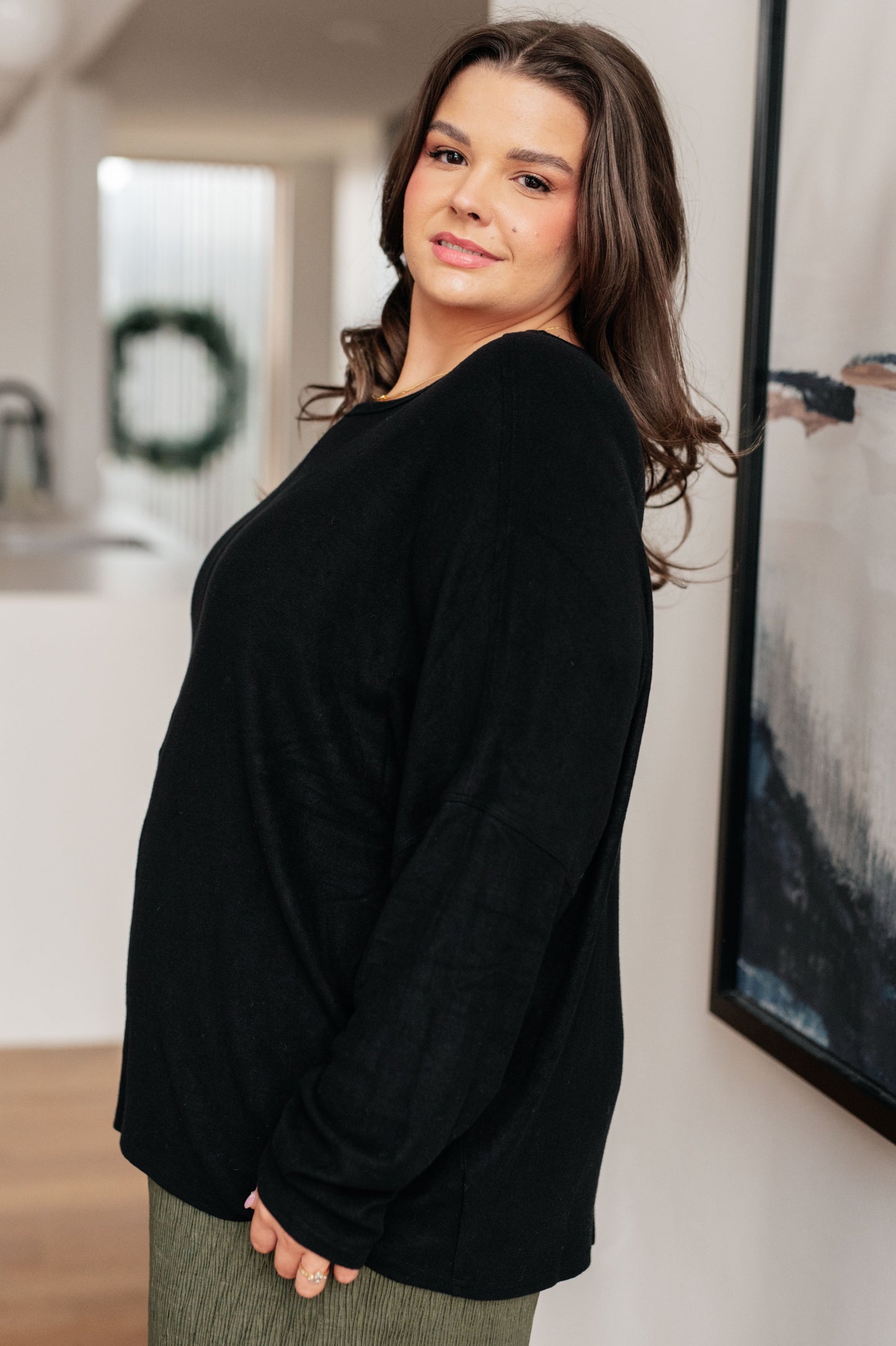 Woman wearing a black sweater standing indoors with a neutral background