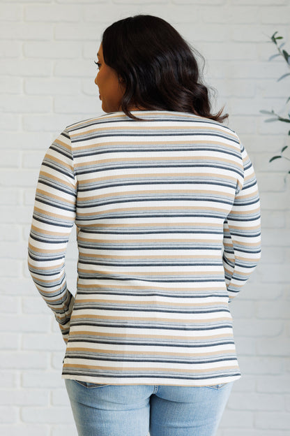 Woman wearing a striped long-sleeve top against a white brick wall.