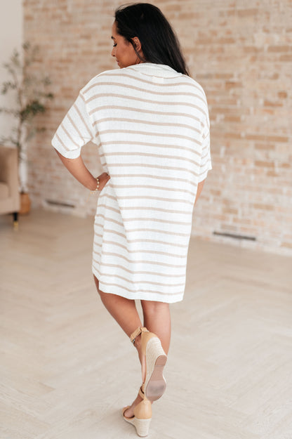 Woman wearing a white and beige striped dress in an indoor setting.