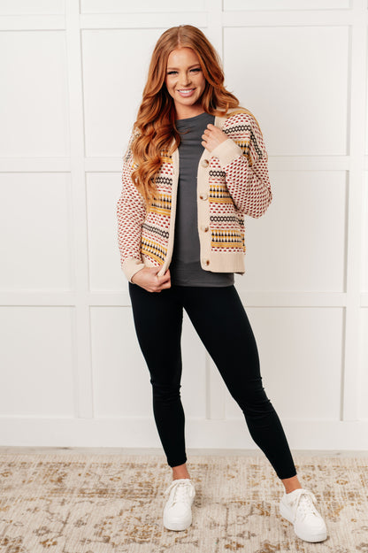 Woman wearing a patterned cardigan, gray shirt, black leggings, and white sneakers against a white wall.