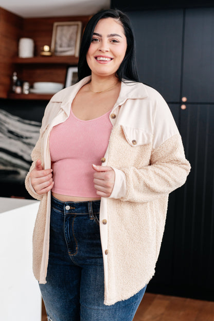 Woman wearing a beige cardigan over a pink top and blue jeans indoors.
