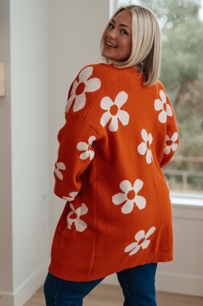Person wearing an orange sweater with white floral patterns indoors.
