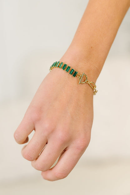 Hand wearing a green beaded bracelet on a plain background