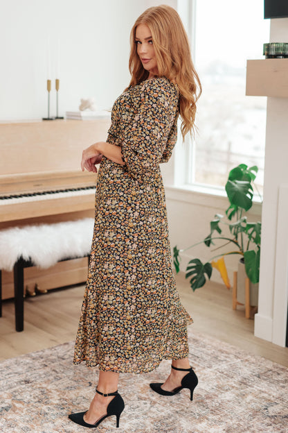 Woman in a floral dress standing in a room with a piano and plants.